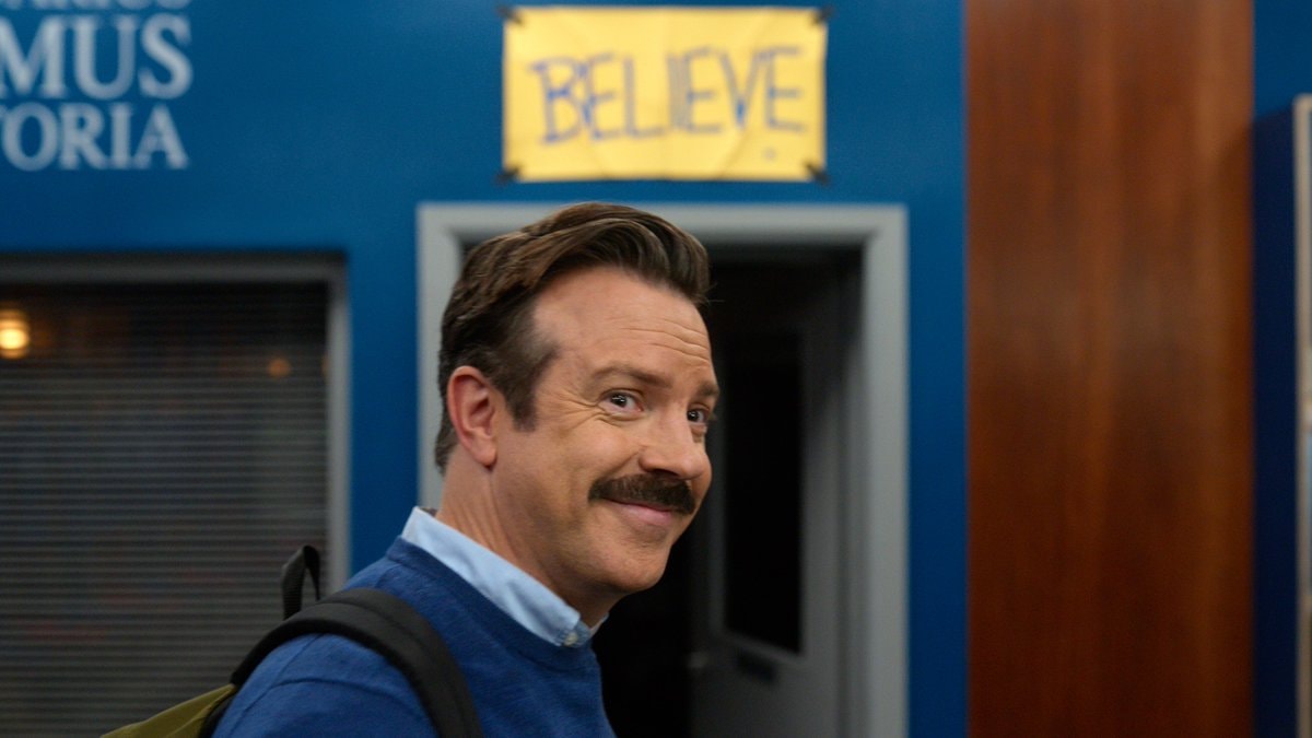 man in blue sweater Believe sign